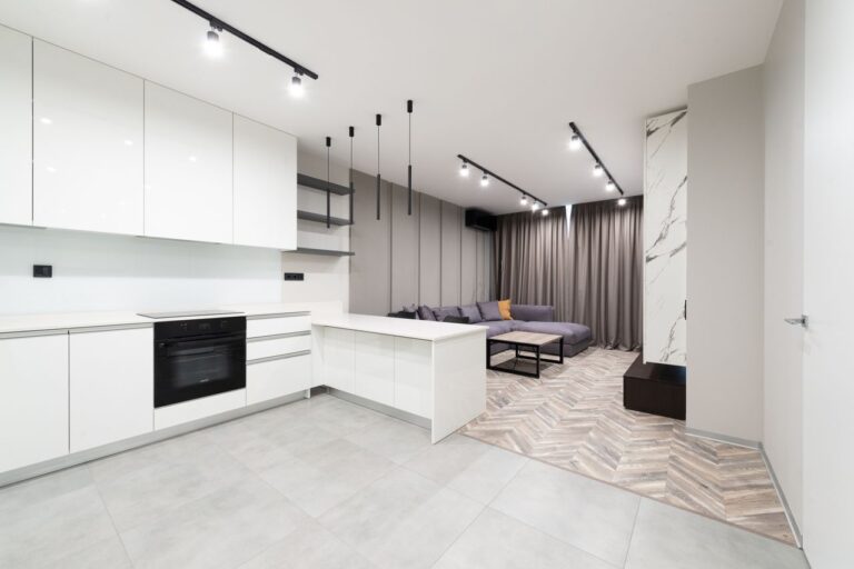 Sleek open-plan kitchen and living area with contemporary design featuring white cabinets and neutral tones.